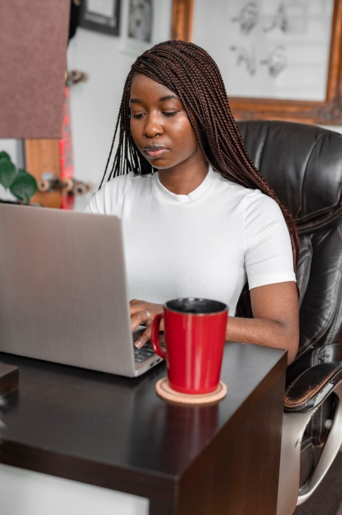 Woman with braids at a desk with a laptop and coffee, researching therapists online